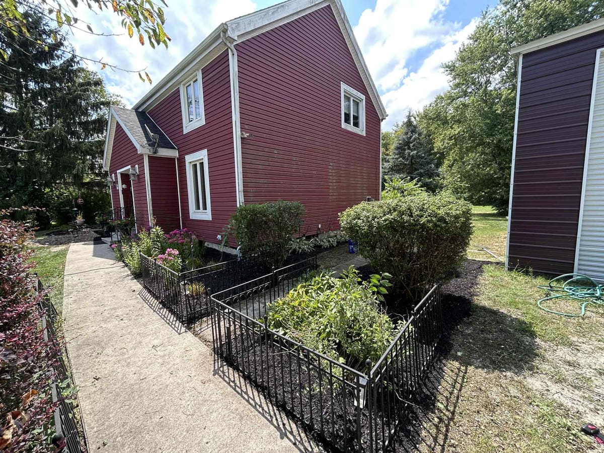 Front walkway with freshly mulched and edged planting beds beside a red house